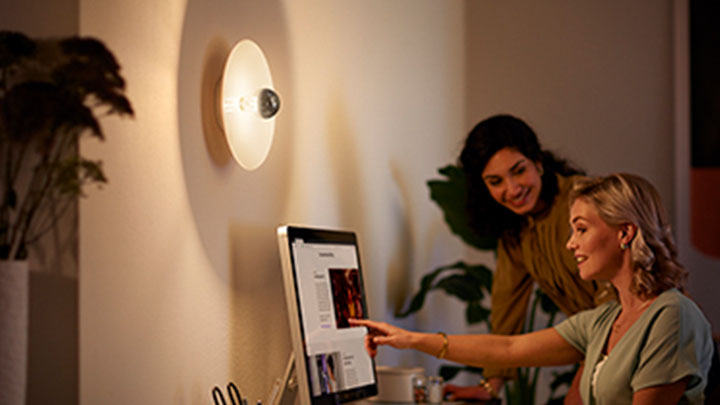 Duvara monte Philips LED ayna ampulünün yanında bilgisayarda çalışan kadınlar