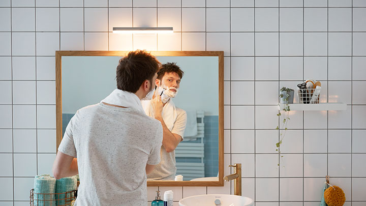 Duvara monte bir Philips LED ile aydınlatılan banyo aynasının karşısında tıraş olan adam