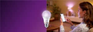 Akıllı LED aydınlatmayı akıllı telefon uygulamasıyla kontrol eden kadın, bağlantılı ev teknolojisiyle donatılmış rahat bir oturma odasında sıcak bir atmosfer yaratıyor.